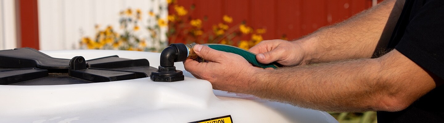 Man attaching a hose to an ABI Attachments 340 Gallon Compact Water Trailer