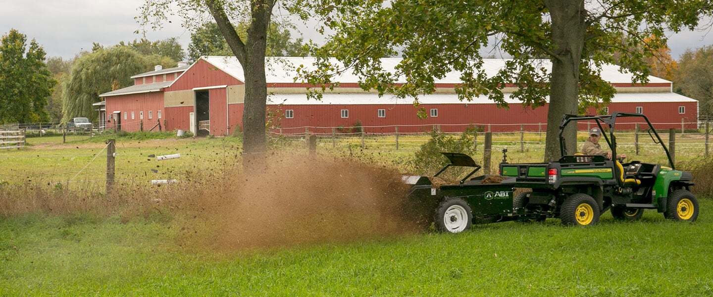 ABI Attachments 50 Cubic Foot Ground Drive Manure Spreader spreading manure on a field