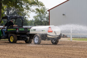 ABI Attachments 340 Gallon Compact Water Trailer spraying water on ground while being pulled by a UTV