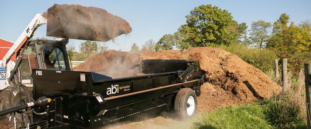 Skid-Steer Loader loading an ABI Attachments 185 Cubic Foot PTO Driven Manure Spreader with steaming manure