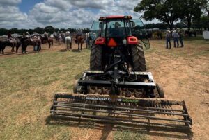 ABI Attachments TR3 Rodeo Arena Drag displayed in front of a rodeo crowd, showcasing rolling basket, adjustable scarifiers, auto-leveling blade.