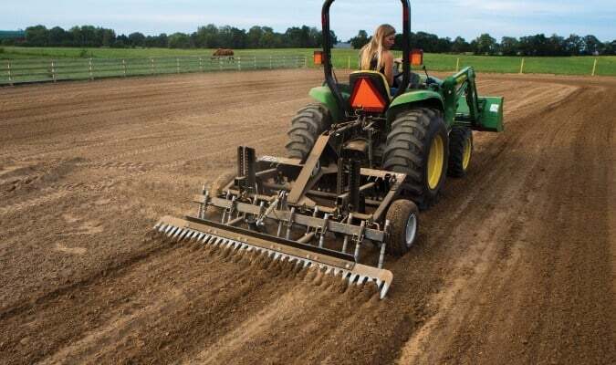 Arena drag being attached to a green tractor on natural footing.