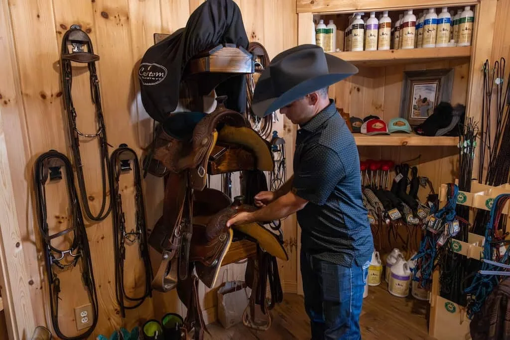 Man with large hat is taking care of saddles in. building.