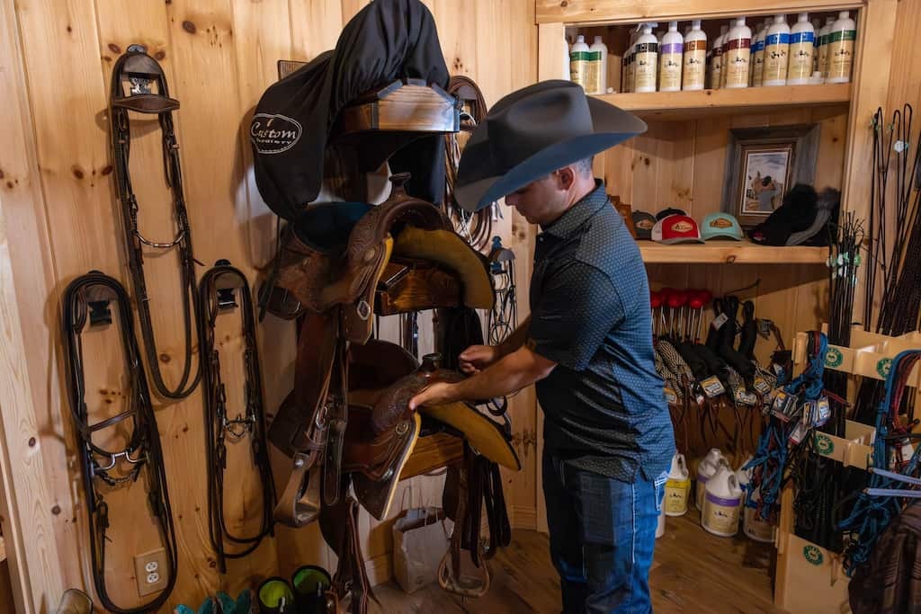 Man with large hat is taking care of saddles in. building.